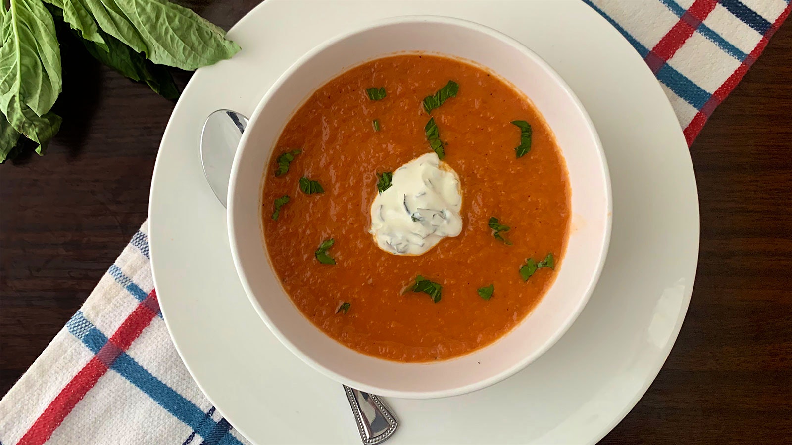 Bowl of tomato soup topped with a dollop of herb crema and sprinkled with chopped fresh basil.